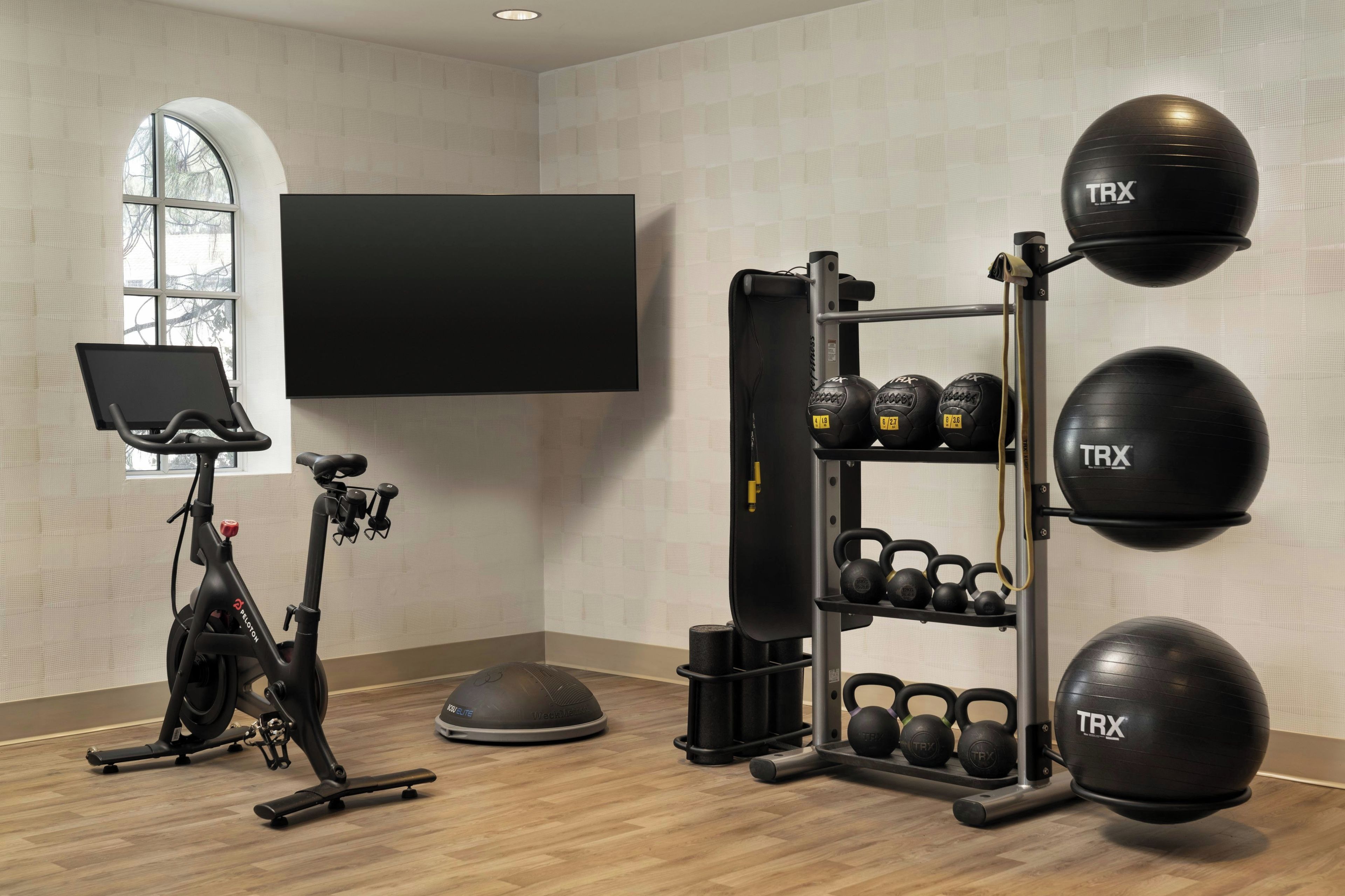 Une salle de sport à domicile équipée d’un vélo elliptique, d’un support pour squats, de sangles de suspension TRX et de kettlebells.