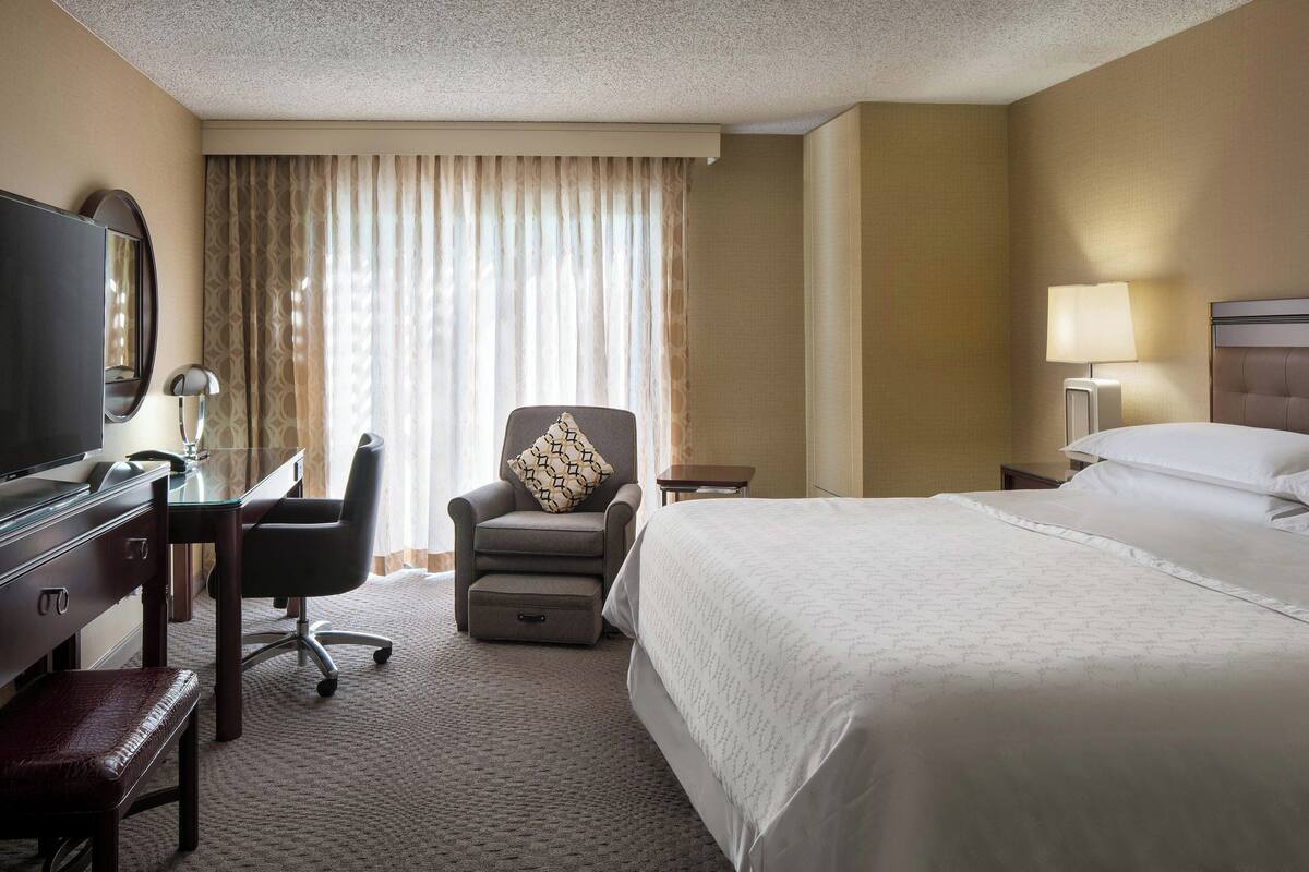 Una habitación de hotel con una cama, un escritorio con silla, televisión y lámpara.