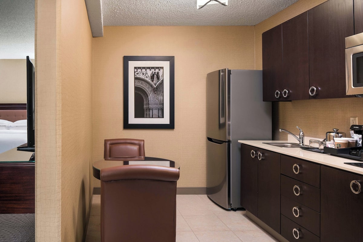 Habitación de hotel compacta con kitchenette, una cama y un cuadro enmarcado en la pared.