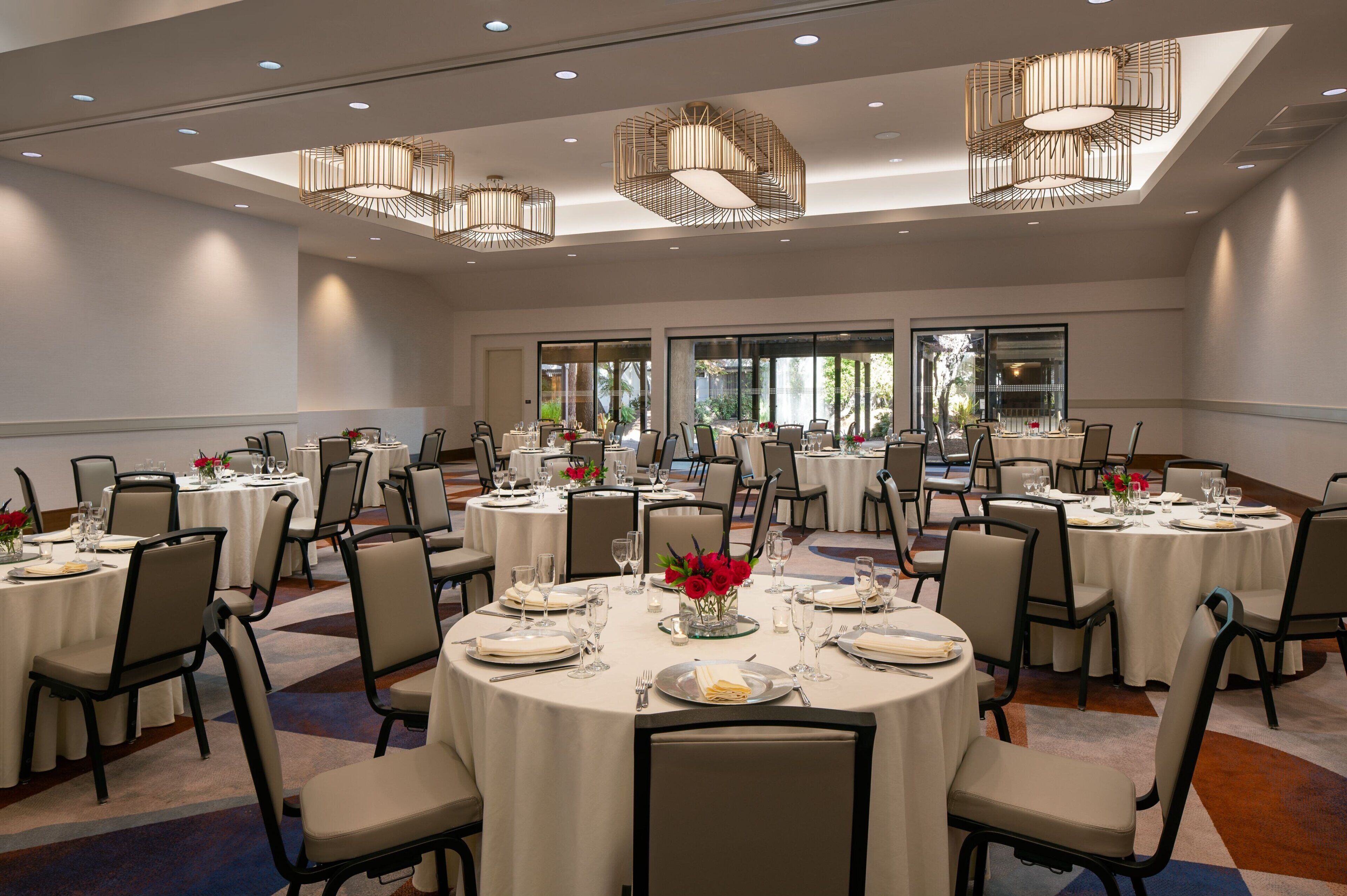 A large conference room with multiple round tables, each set with white tablecloths, chairs, and glassware.