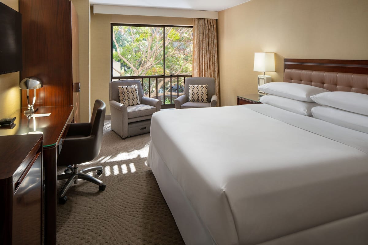 Una habitación de hotel con una cama grande, dos sillones, un escritorio y un televisor.