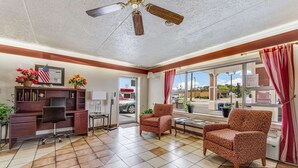 A spacious room with a desk, two patterned armchairs, a ceiling fan, and a large window with curtains. - Econo Lodge (Eden)
