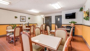 A dining area with multiple tables and chairs, a television mounted on the wall, and potted plants. - Econo Lodge (Eden)