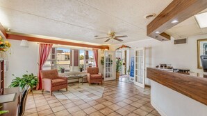 A hotel lobby with a reception desk, two patterned armchairs, a ceiling fan, and a tiled floor. - Econo Lodge (Eden)