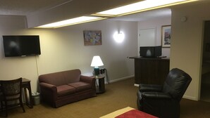A hotel room with a sofa, a chair, a TV, a lamp, and a microwave. - Econo Lodge (Eden)