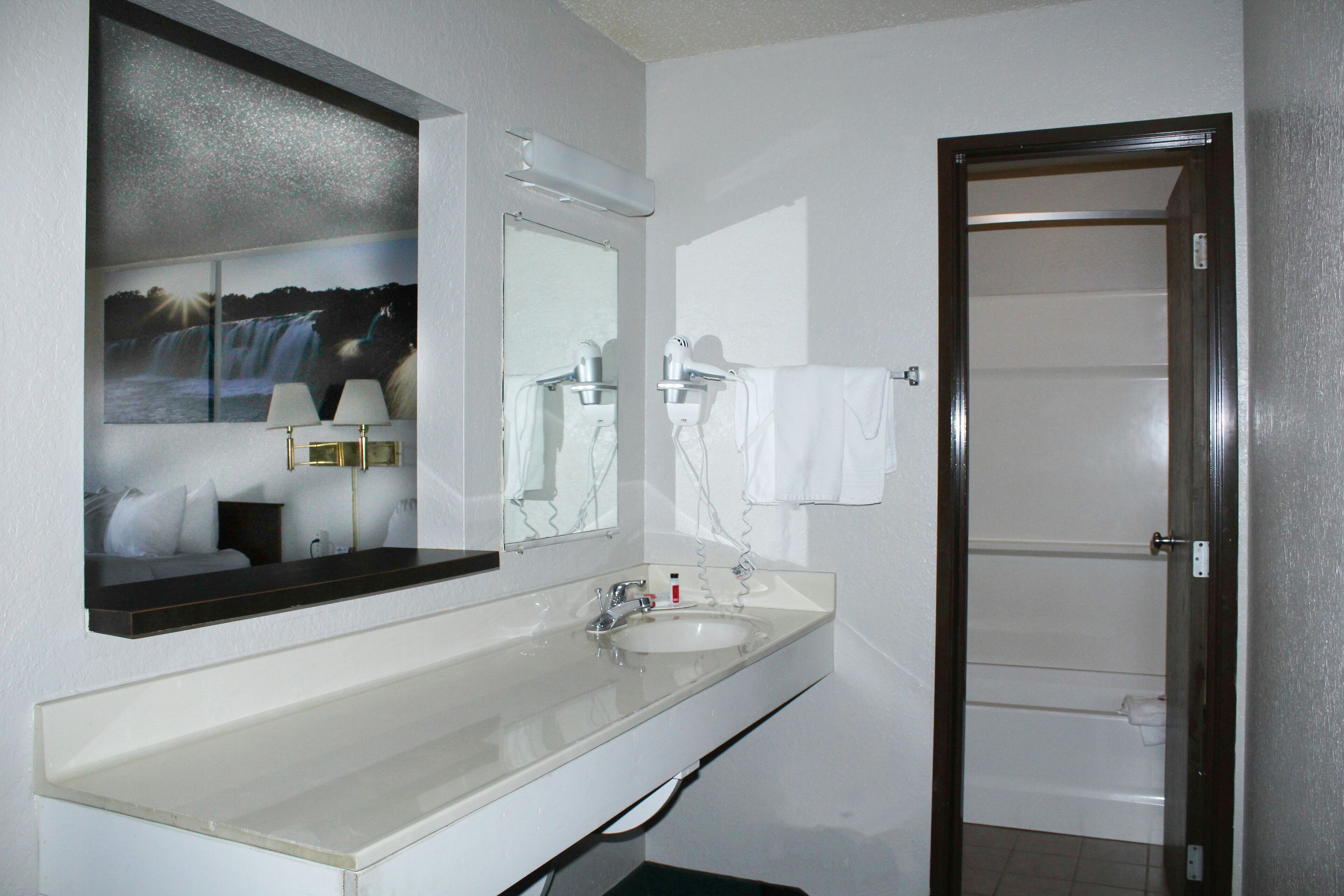 A bathroom with a large mirror, a sink, a hairdryer, and a towel rack.