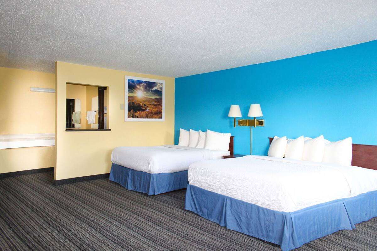 A hotel room with two beds, a mirror, a painting, and a lamp.
