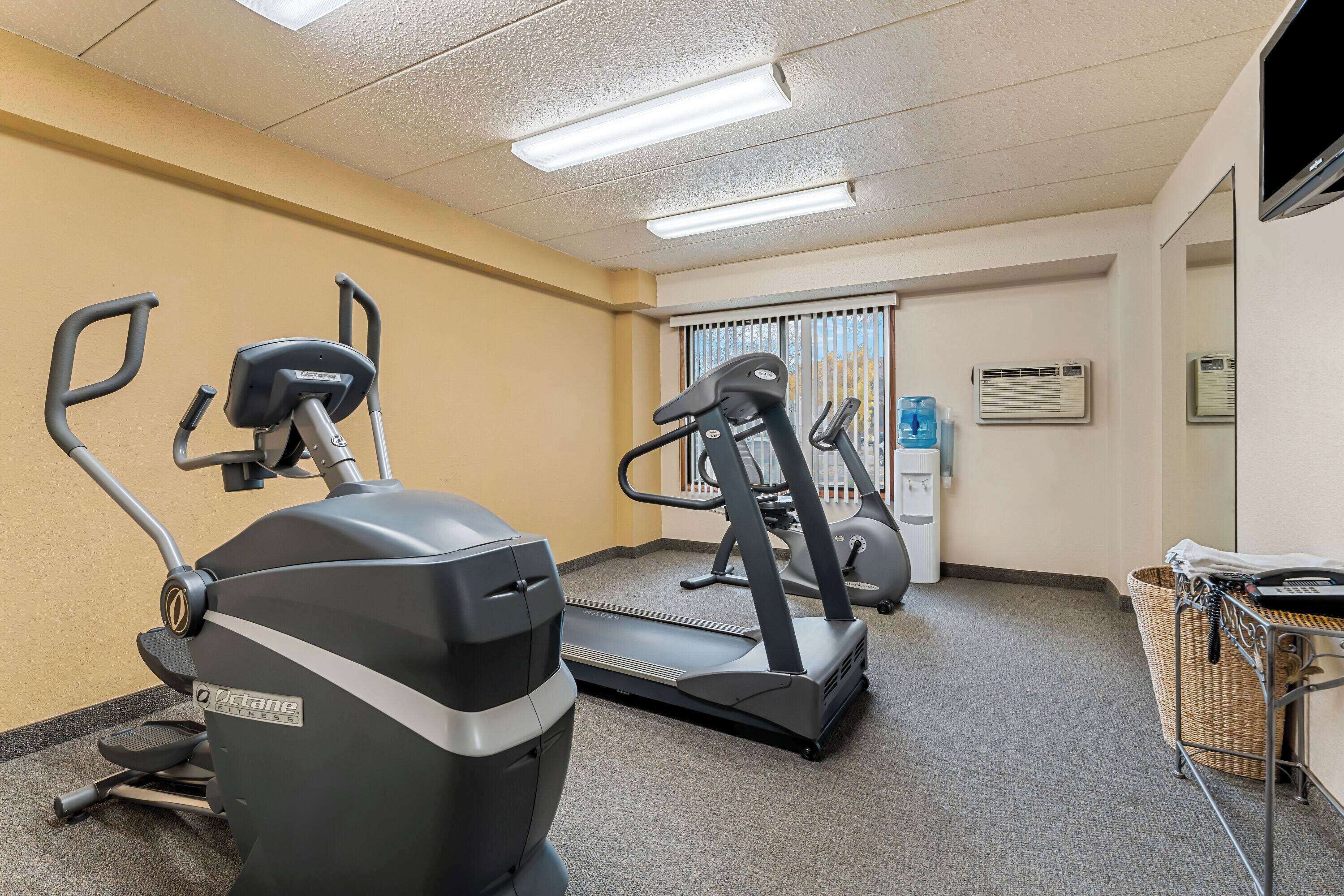 Ein Fitnessraum mit Laufbändern, einem Crosstrainer, einem Wasserspender und einem Mülleimer.