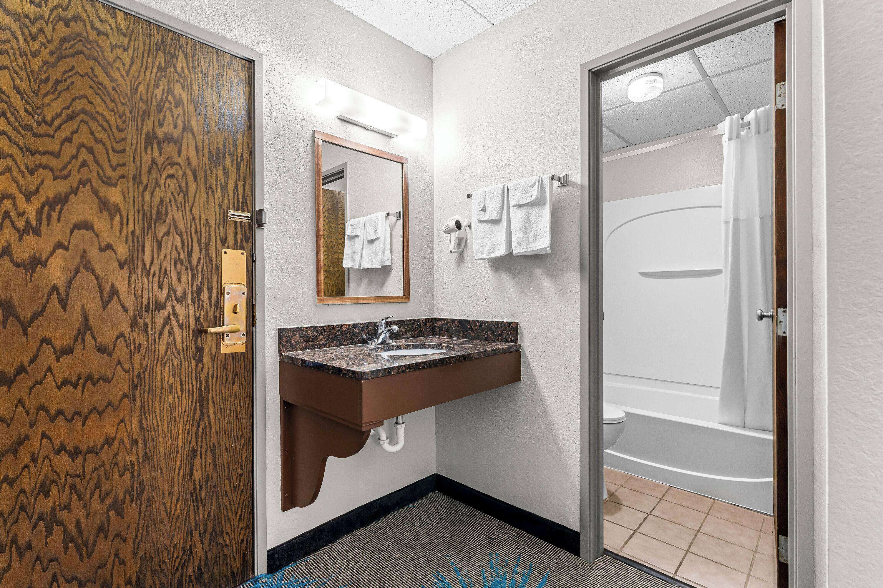 Un baño con puerta de madera, un lavabo con espejo y zona de ducha.