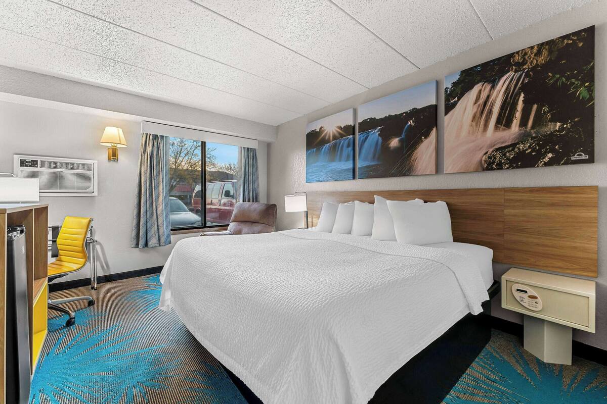 A hotel room with a large bed, a desk with a chair, a window with curtains, and a wall-mounted TV.