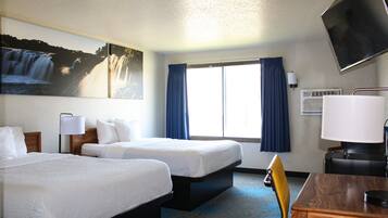 A hotel room with two beds, a desk, a chair, a TV, and a window with curtains.