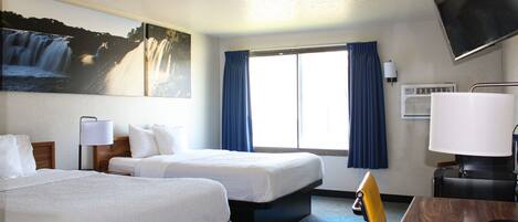 A hotel room with two beds, a desk, a chair, a TV, and a window with curtains.