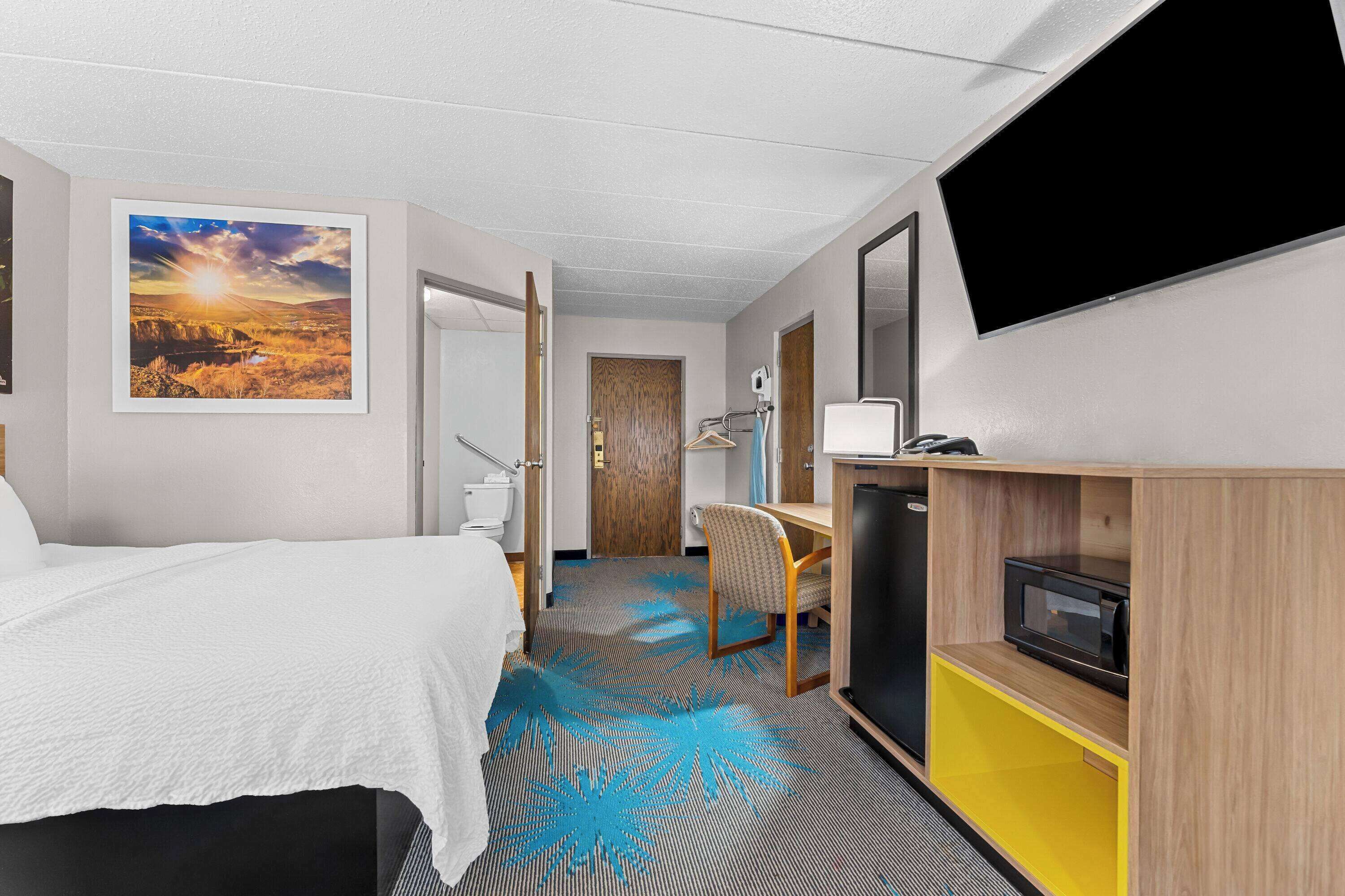 A hotel room with a bed, a desk, a TV, and a bathroom visible through an open door.