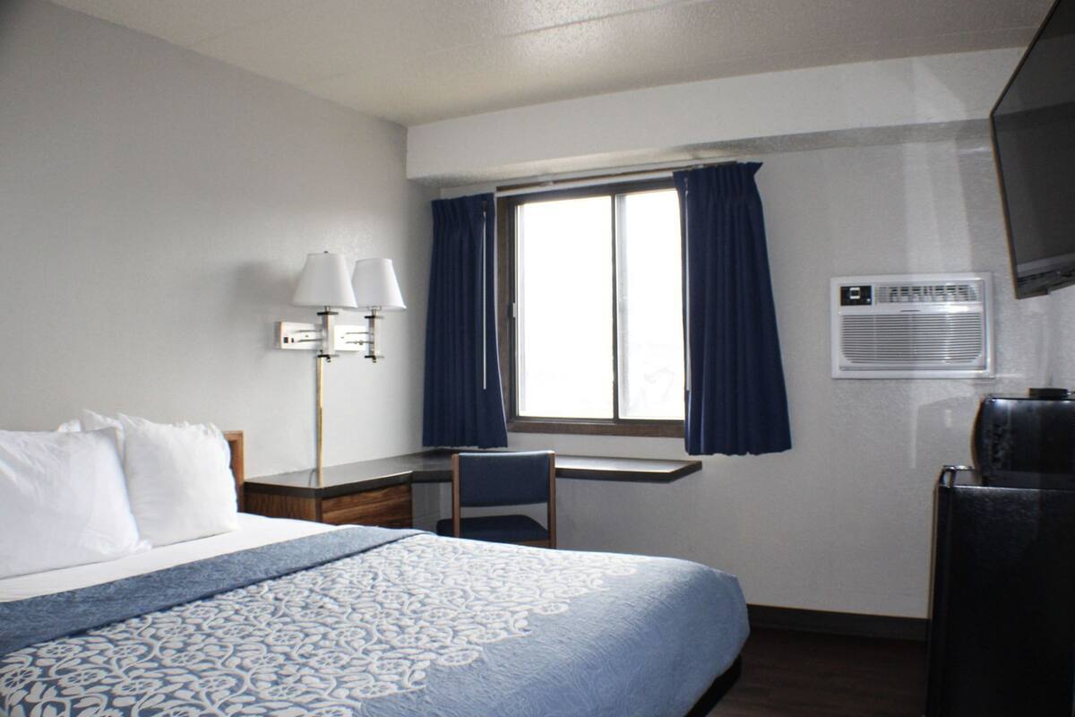 A hotel room with a bed, desk, chair, and a television.