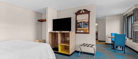 A hotel room with a bed, a TV, a small desk, a chair, and a window with curtains.