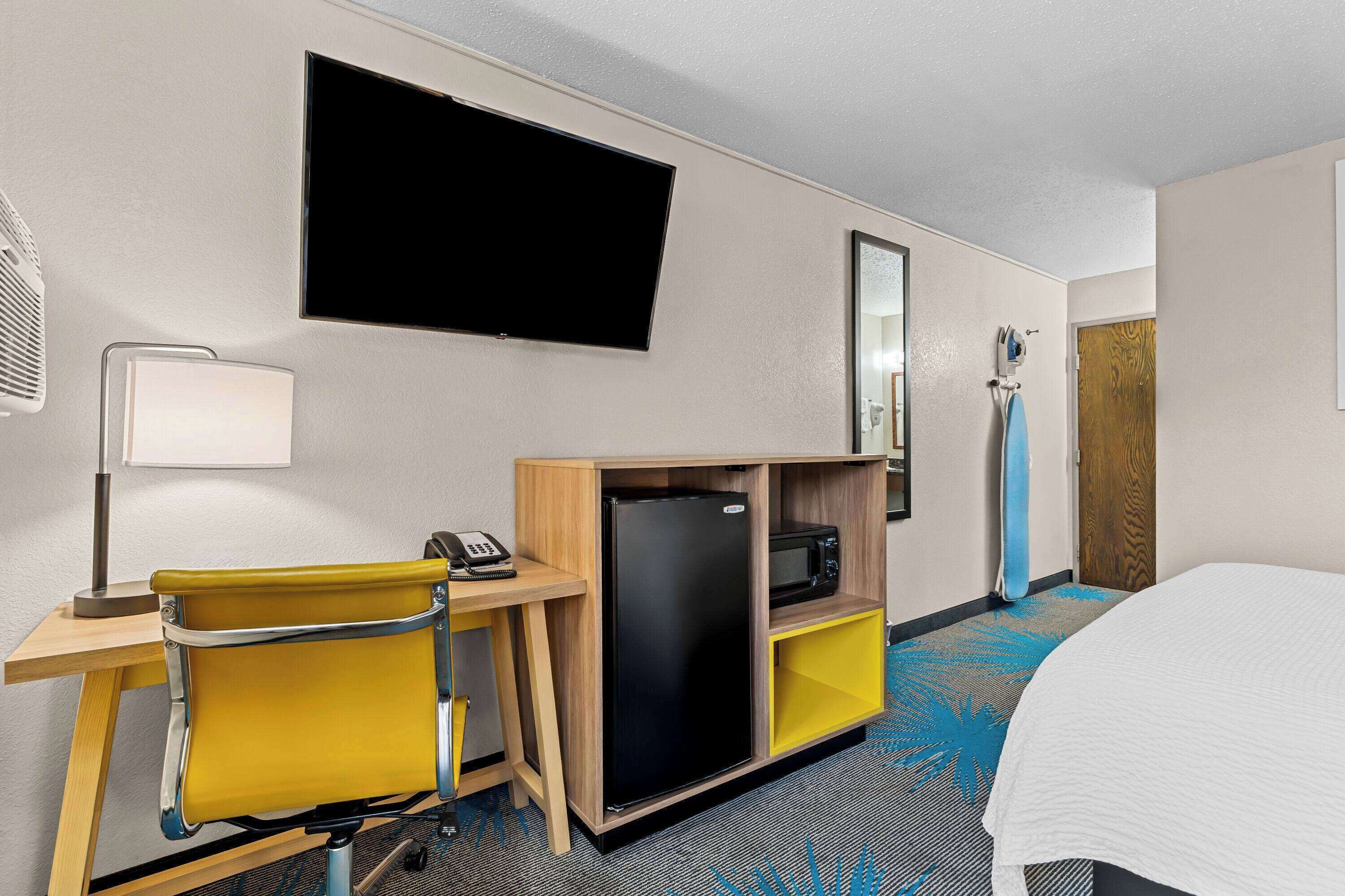 A hotel room with a bed, a desk with a chair, a television, a refrigerator, a microwave, and a bathroom with a shower.