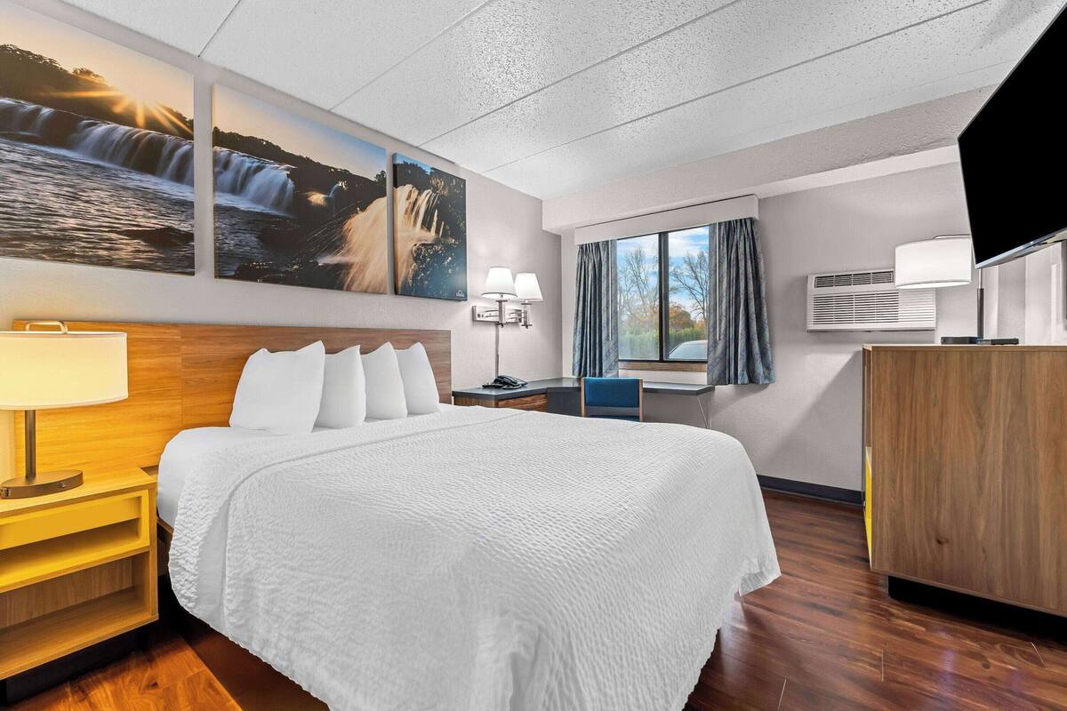 A hotel room with a large bed, a desk, a chair, a TV, and a window with curtains.