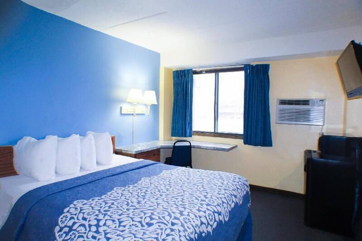 A hotel room with a bed, desk, chair, and window with curtains.