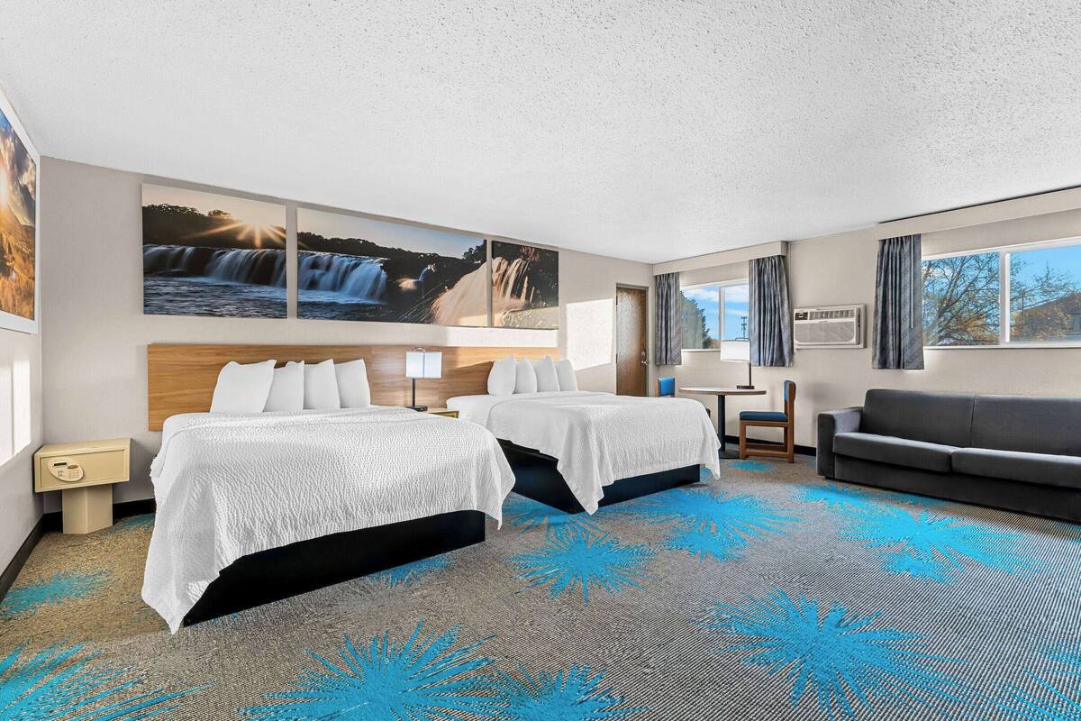 A hotel room with two beds, a sofa, a desk, and a large window.