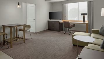 Habitación de hotel con escritorio, dos sillas, un sofá, televisor y ventana con cortinas.