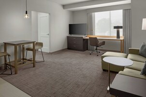 Habitación de hotel con escritorio, dos sillas, un sofá, televisor y ventana con cortinas.