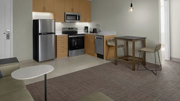 Una cocina compacta con electrodomésticos modernos, un comedor con una mesa pequeña y dos sillas, y una puerta a la vista.