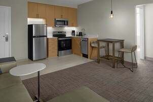 Una cocina compacta con electrodomésticos modernos, un comedor con una mesa pequeña y dos sillas, y una puerta a la vista.