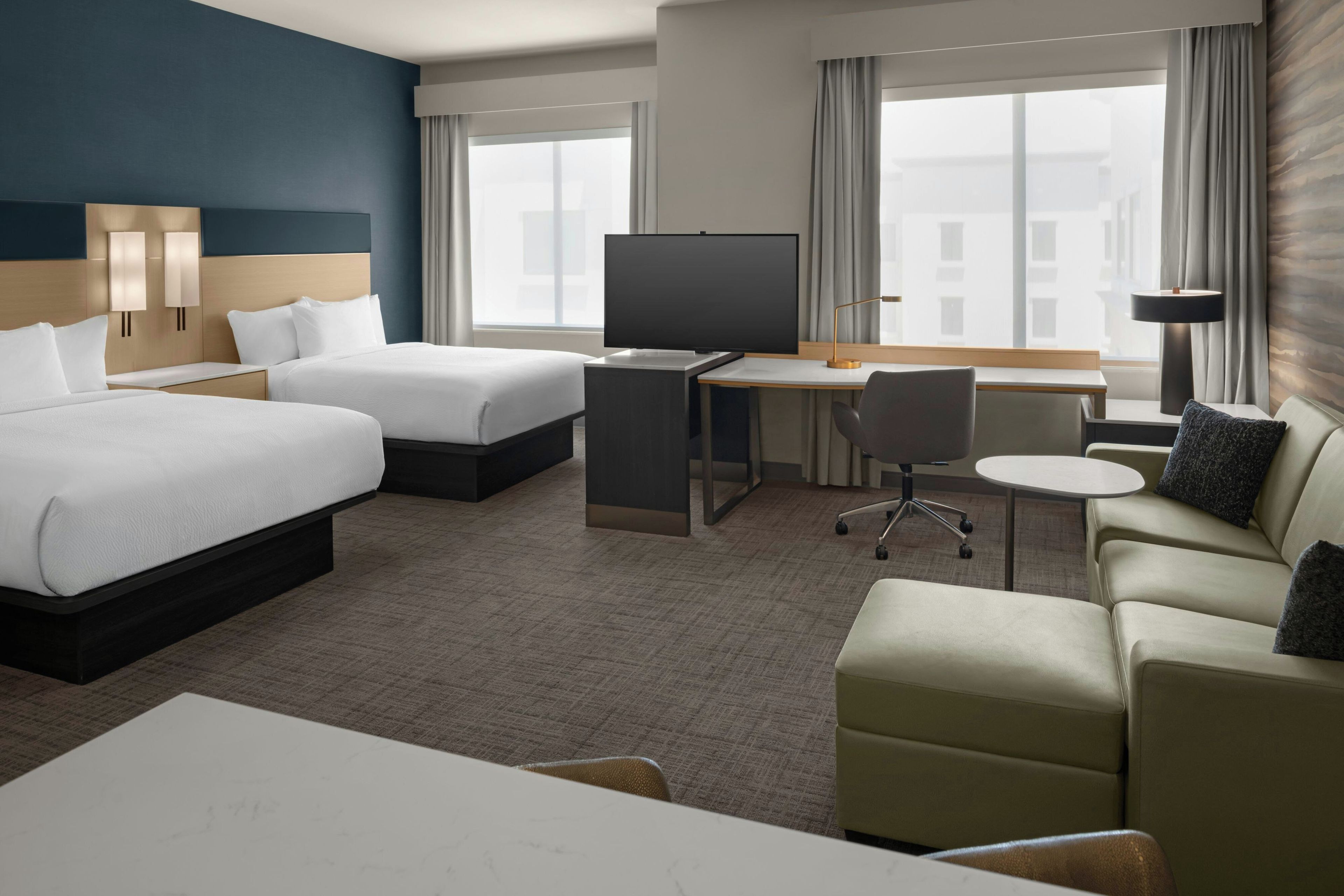 A hotel room with a bed, two bedside tables, a desk with a chair, a television, and a sofa.