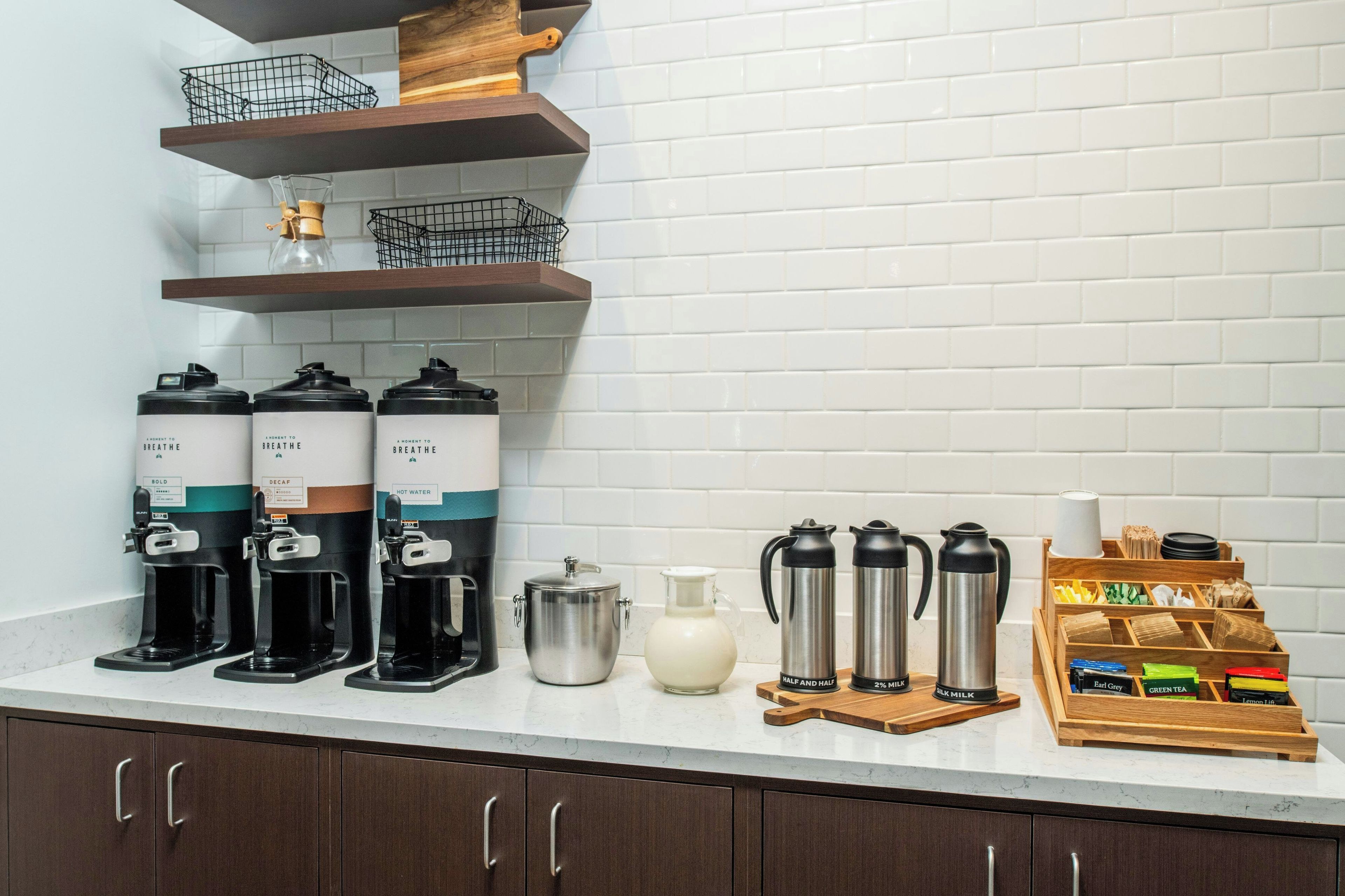 Eine Küchenzeile mit Kaffeeautomaten, einer Milchkaraffe und einer Teeausstattung.
