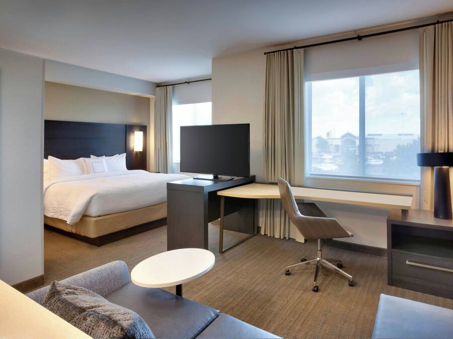 Una habitación de hotel moderna con cama, escritorio, silla y un ventanal con vistas.