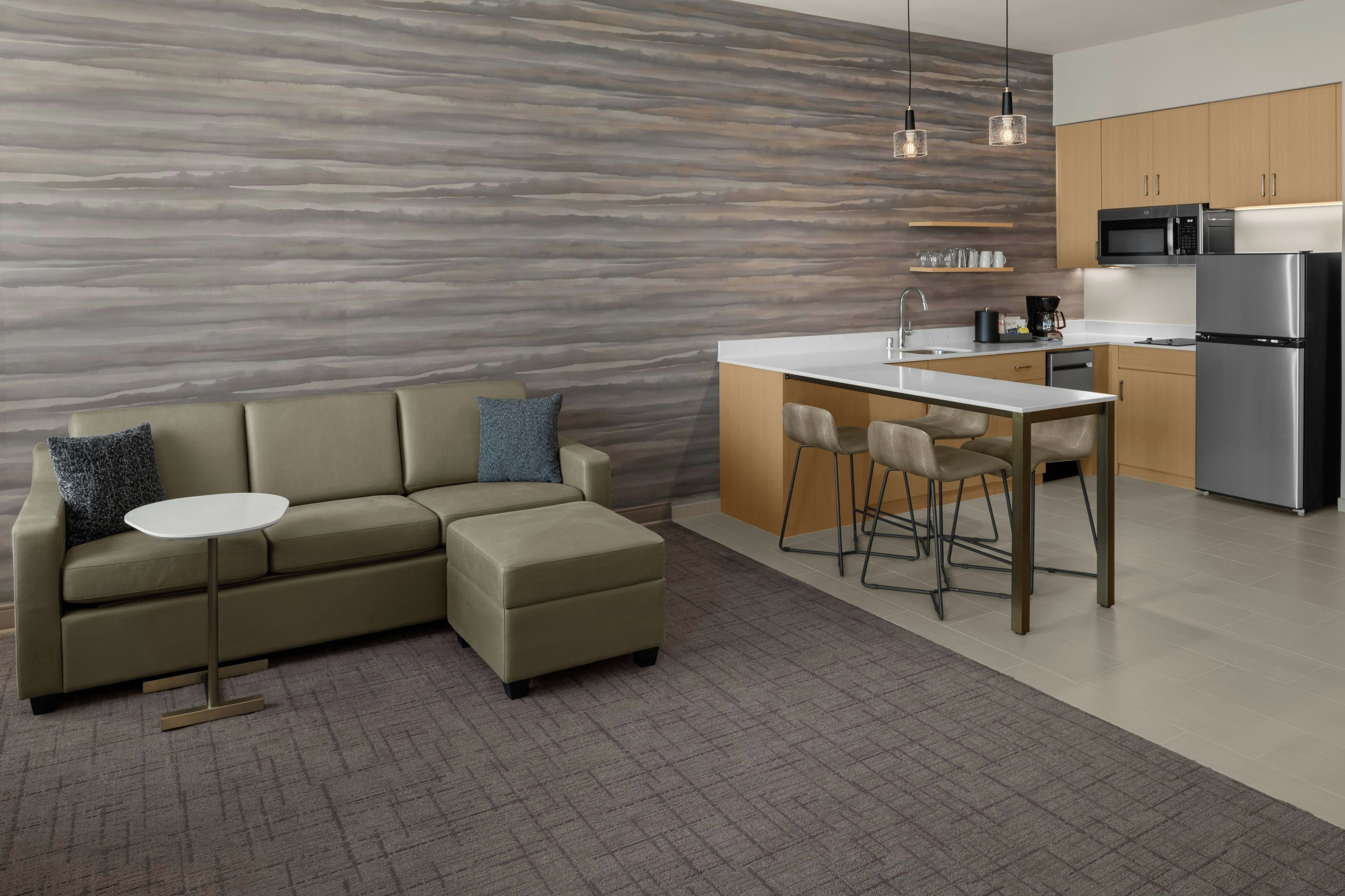 A modern kitchen with a built-in microwave, refrigerator, and bar stools.