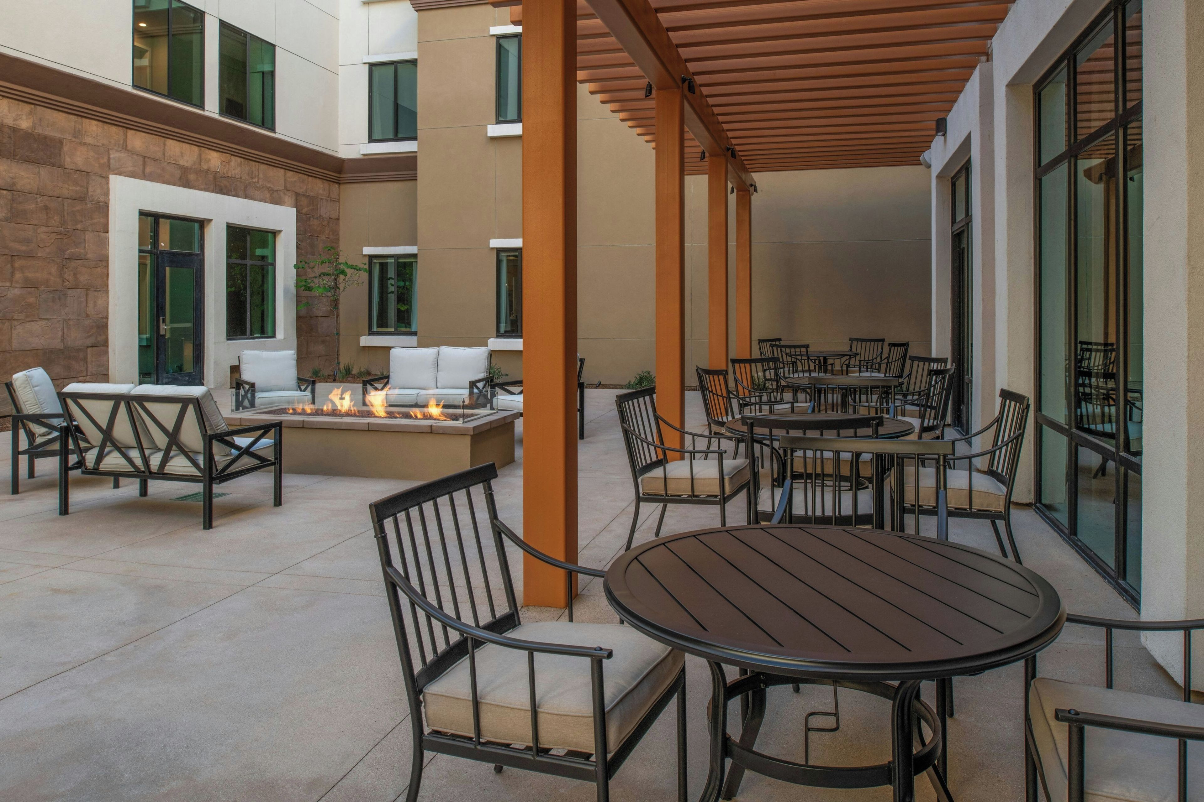 An outdoor patio with round tables and chairs, a fire feature, and a covered seating area.