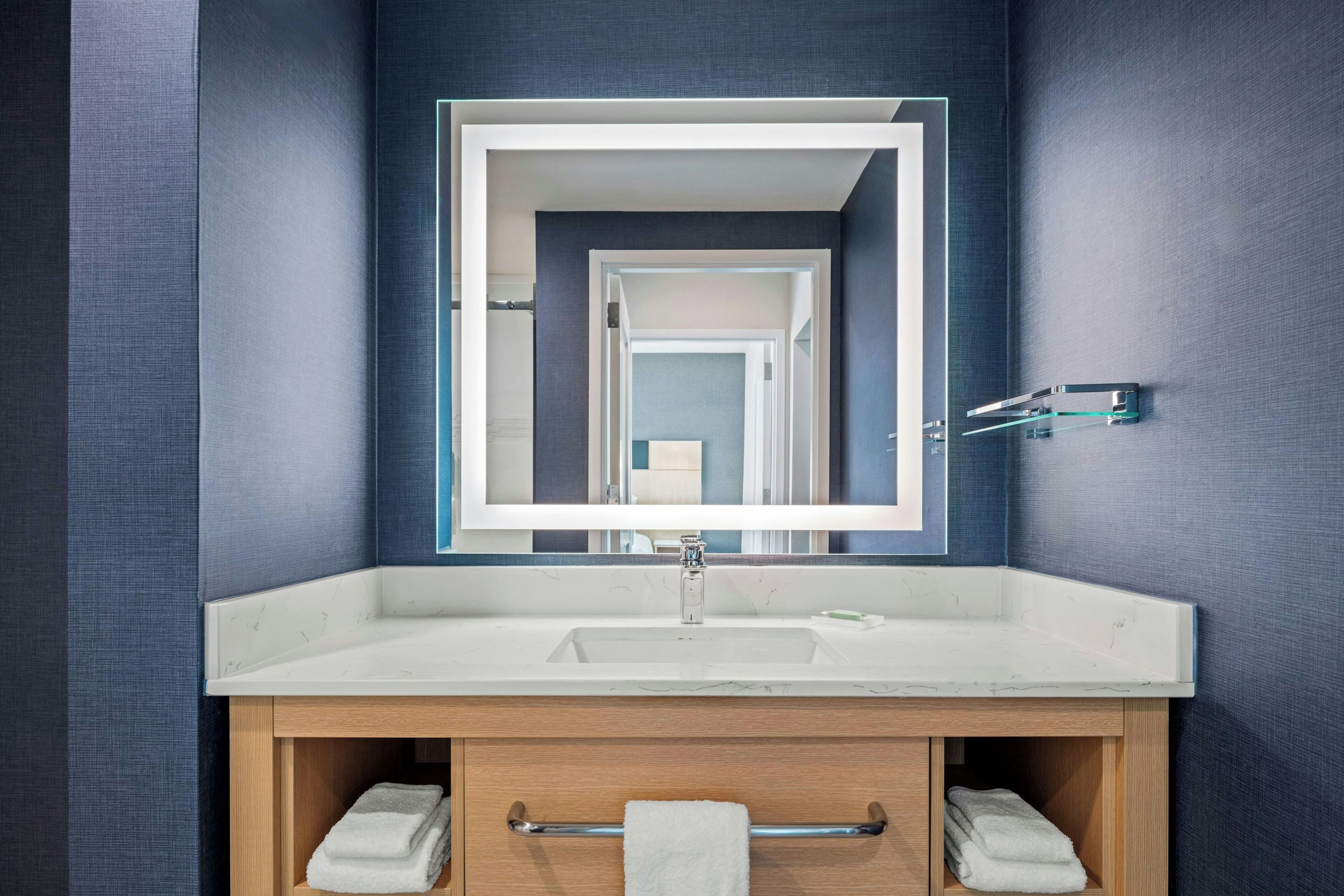 A modern bathroom with a large mirror, a white sink, and a wooden vanity.