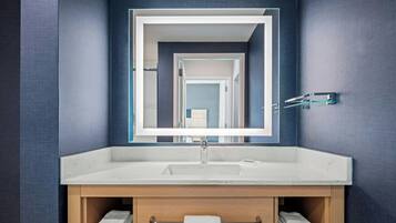 A modern bathroom with a large mirror, a white sink, and a wooden vanity.