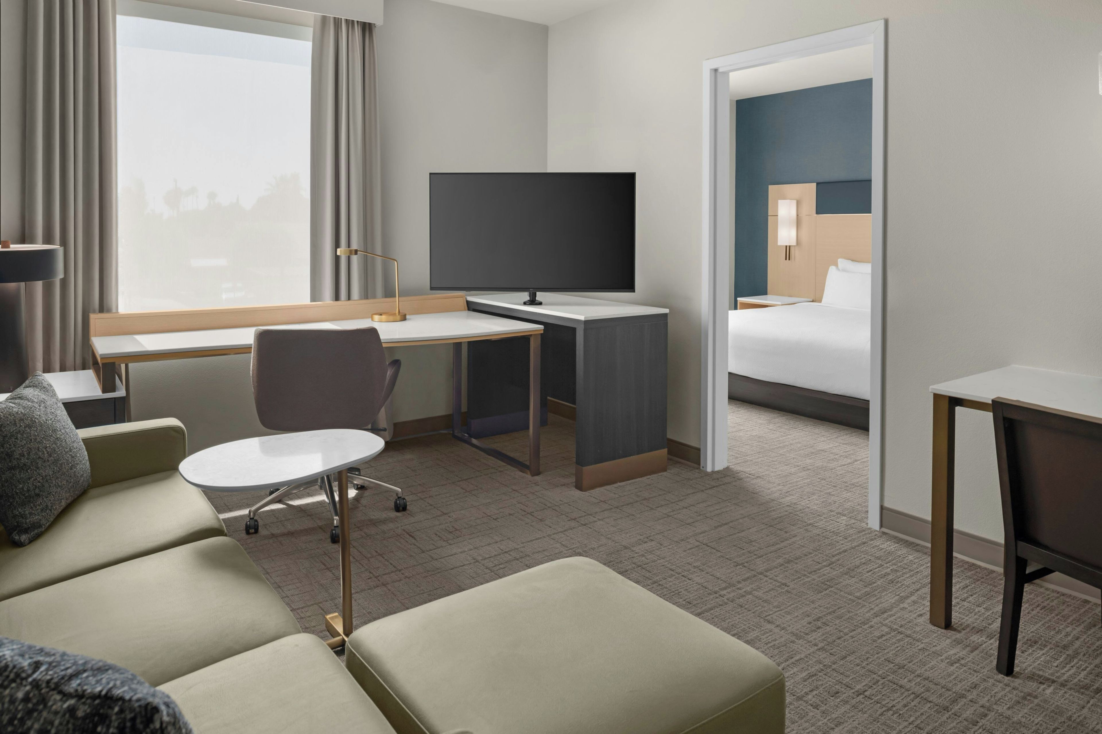 A hotel room with a bed, a desk, a chair, a TV, and a sofa.