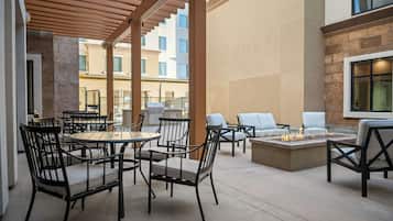 Un área de patio al aire libre con mesas y sillas redondas, una chimenea y vistas del exterior del edificio.