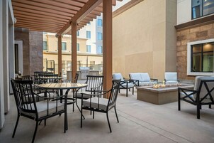 Un área de patio al aire libre con mesas y sillas redondas, una chimenea y vistas del exterior del edificio.