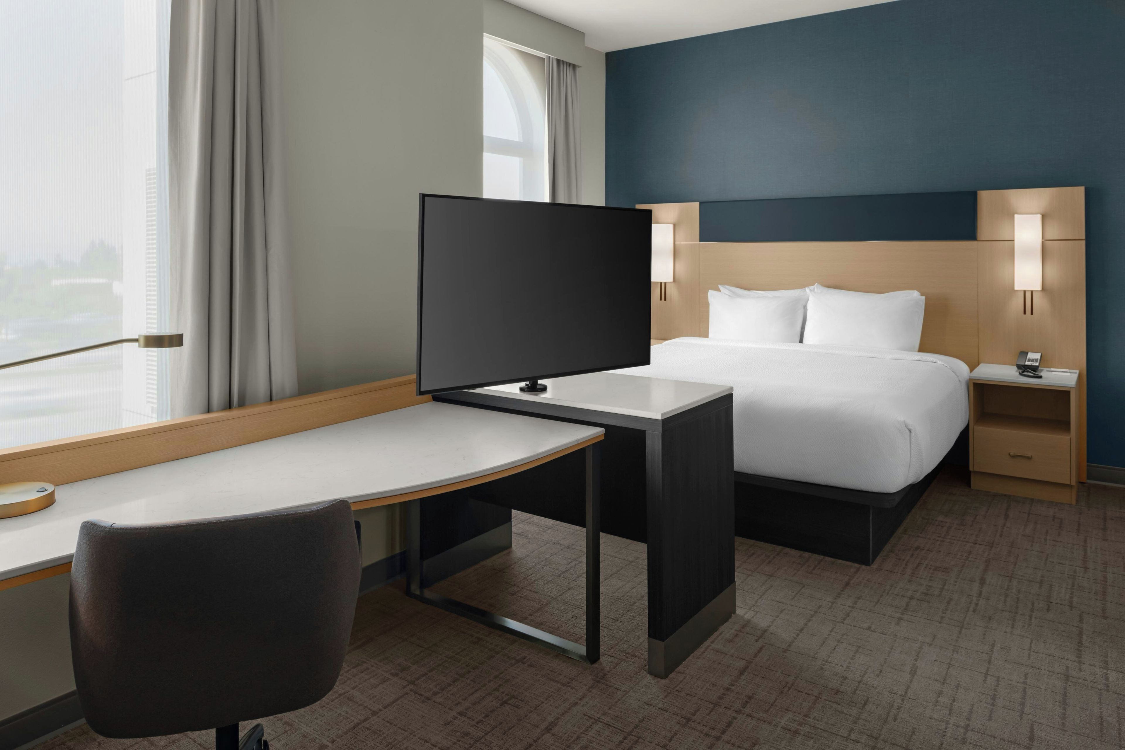 Una habitación de hotel con una cama, un escritorio, una silla, un televisor y una mesita de noche con lámpara.