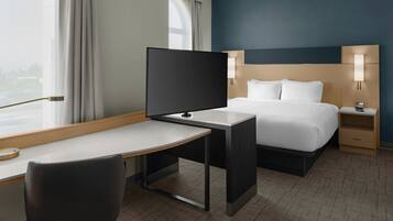 Una habitación de hotel con una cama, un escritorio, una silla, un televisor y una mesita de noche con lámpara.