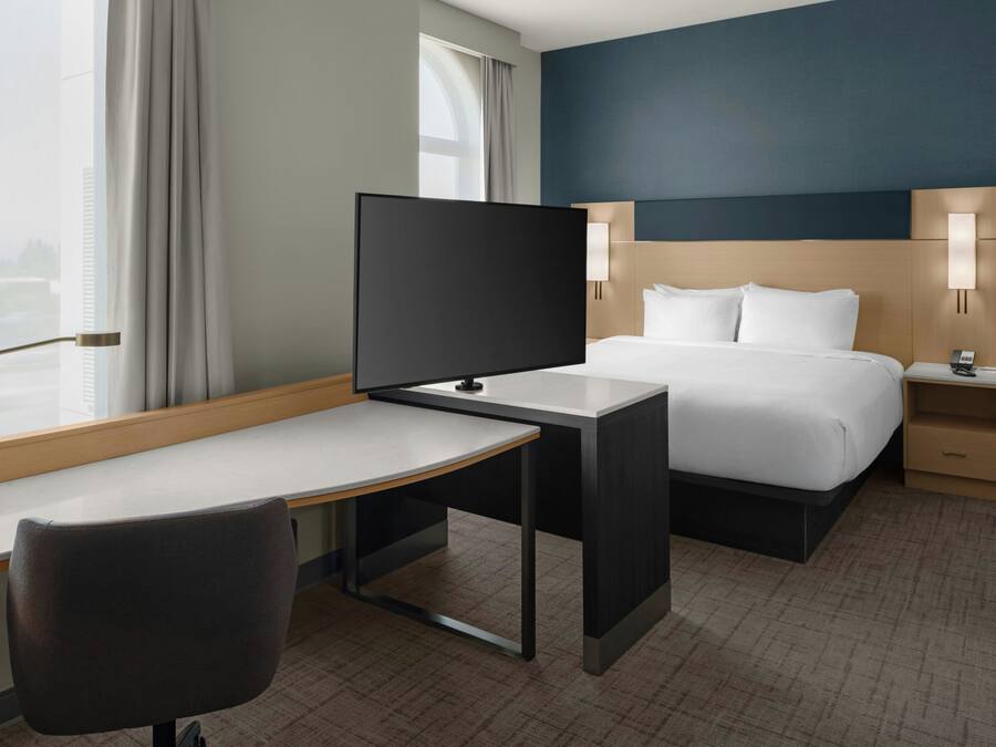 Una habitación de hotel con una cama, un escritorio, una silla, un televisor y una mesita de noche con lámpara.