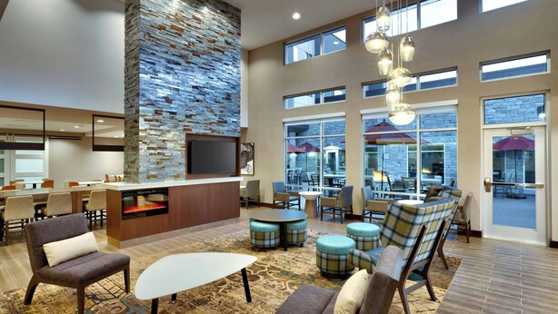 Un'ampia hall con una parete decorata in pietra, diverse zone relax e ampie finestre che garantiscono luce naturale.
