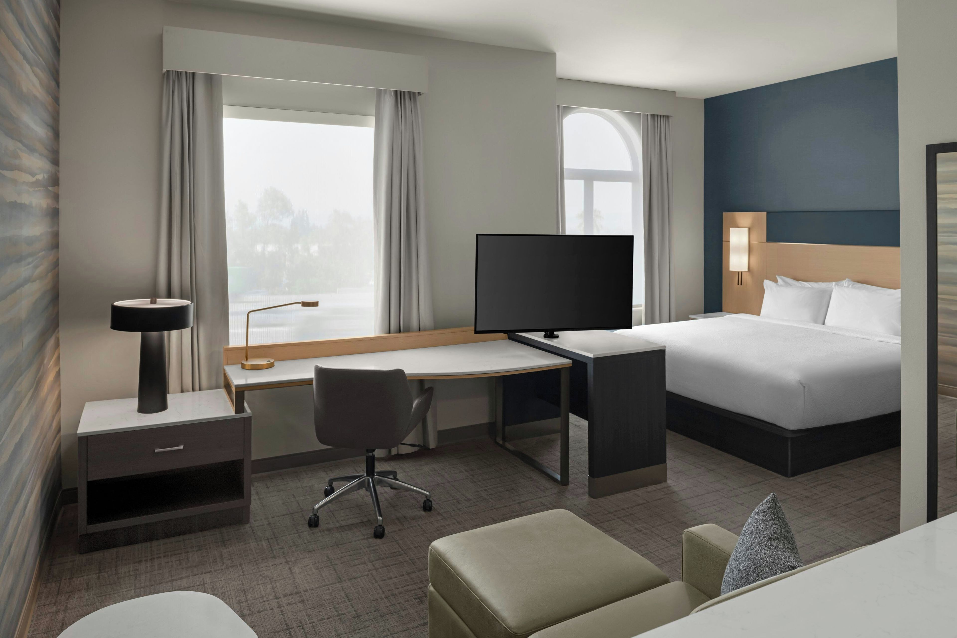 A hotel room with a bed, desk, chair, TV, and a window with curtains.