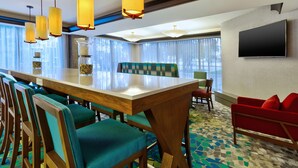 A hotel room with a wooden dining table, teal upholstered chairs, a red sofa, and a flat-screen TV mounted on the wall. - Hampton Inn Traverse City (Traverse City)