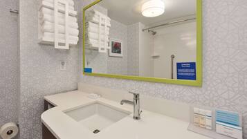 Een moderne badkamer met een wit wastafeltje, een grote spiegel met een groene lijst en een handdoekrek met netjes opgevouwen handdoeken.