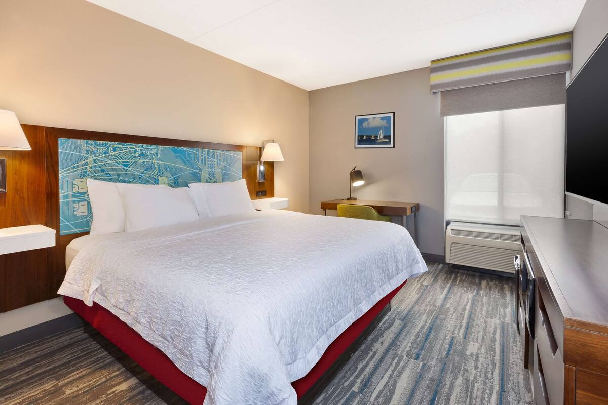 A hotel room with a large bed, a desk, a chair, a TV, and a window.