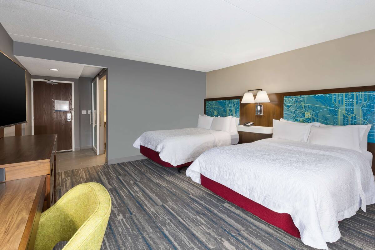 A hotel room with two beds, a desk, a chair, and a television.