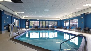 An indoor swimming pool with a blue tiled edge, a lifeguard stand, and multiple chairs along the poolside. - Hampton Inn Traverse City (Traverse City)