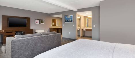 Hotelkamer met een groot bed, een televisie, een bank, een bureau en een badkamer die door een open deur zichtbaar is.