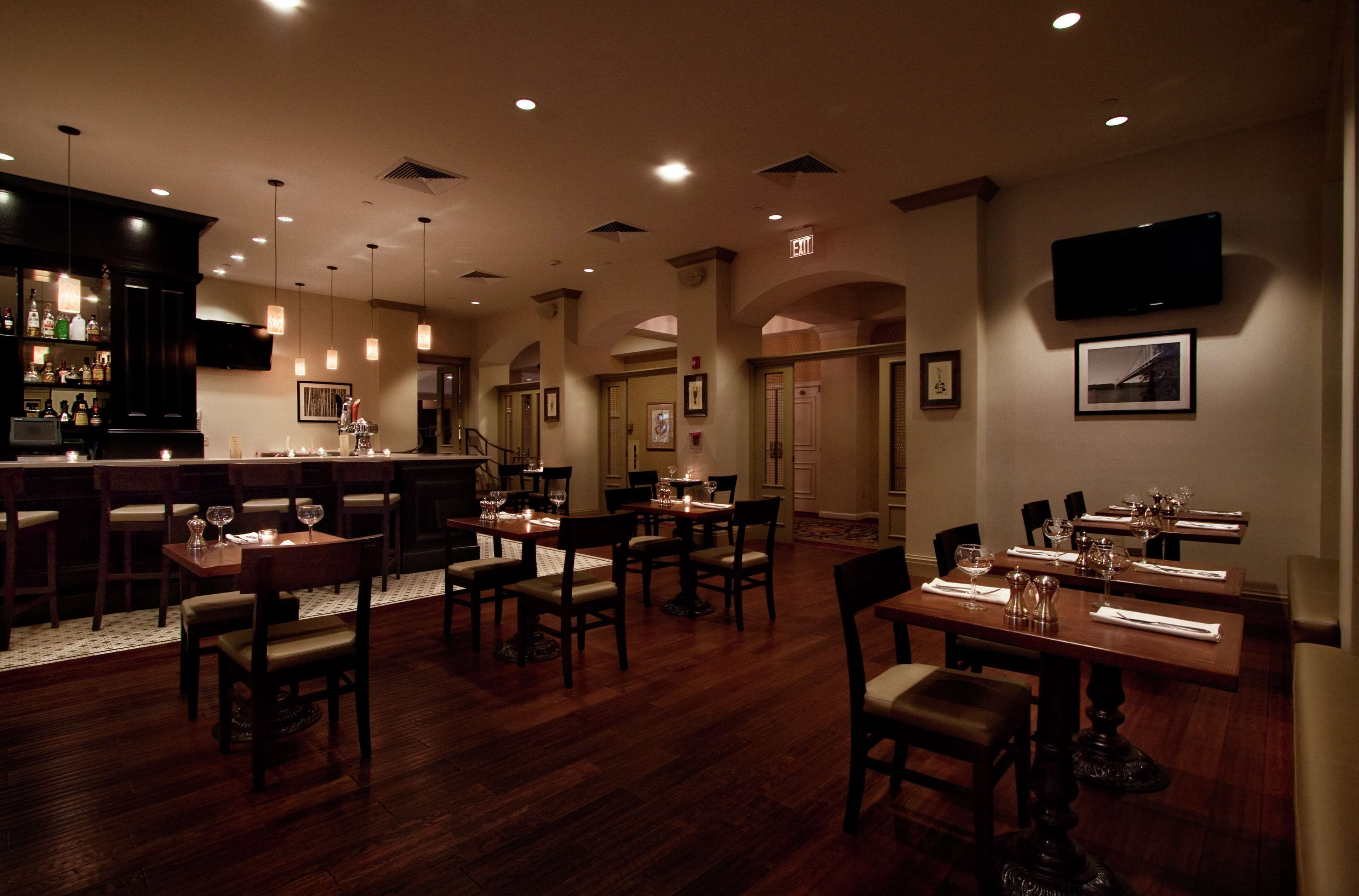A restaurant with wooden tables and chairs, a bar area, and a television mounted on the wall.