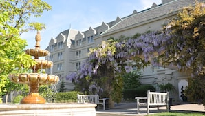 A fountain with multiple tiers, benches, and a building with a distinctive architectural style and purple flowering vines. - Hilton Pearl River (Pearl River)